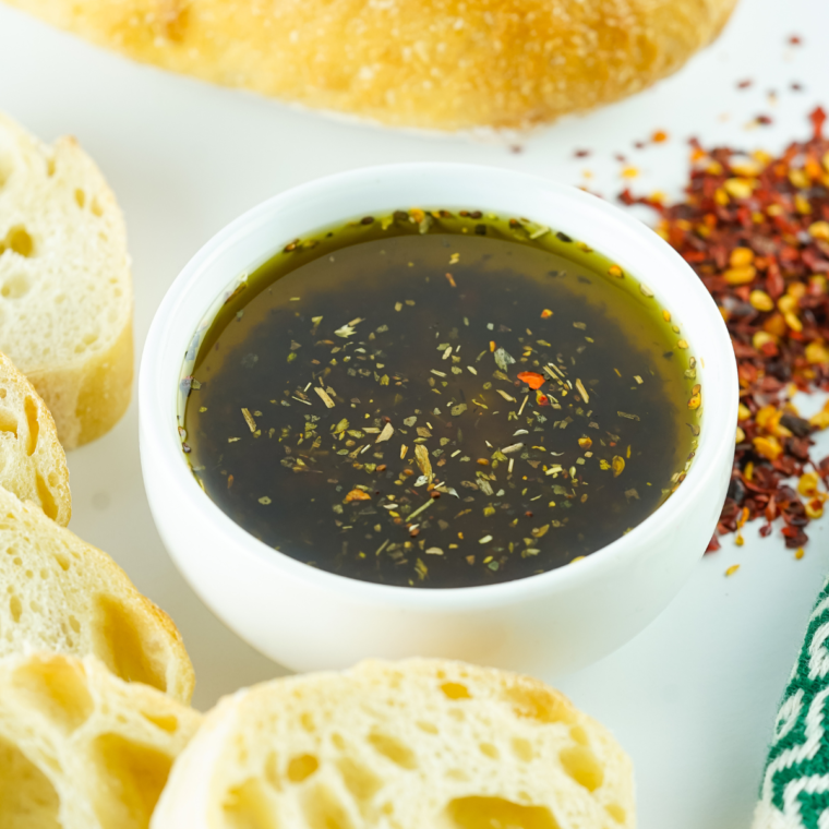 A bowl of 10-minute Mediterranean bread dipping oil with olive oil, garlic, and fresh herbs served with warm bread for dipping.