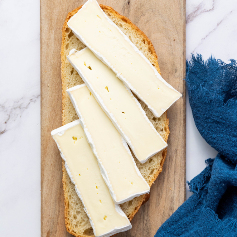 Two slices of bread topped with Brie cheese and crispy bacon, ready for sandwich assembly.