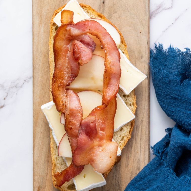 Layer of thinly sliced apples and a drizzle of honey on bacon-topped bread, ready to complete the sandwich.