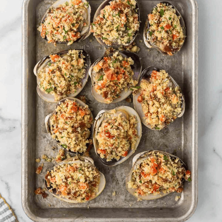 A close-up of spooning the breadcrumb mixture onto clams, topped with crispy bacon pieces for added flavor and texture.