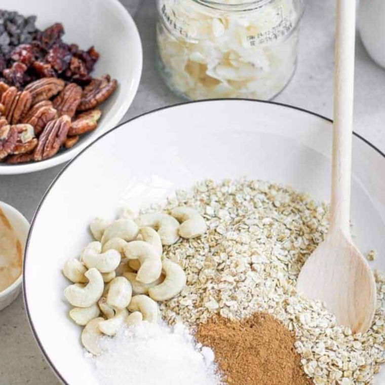 Pouring wet ingredients over dry oats and nuts mixture, stirring to evenly coat for air fryer granola.