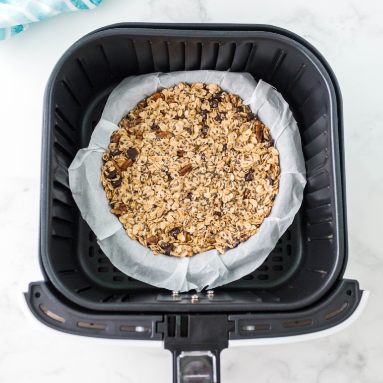 Preheating air fryer to 300°F, lining basket with parchment paper, and spreading granola mixture for even cooking.