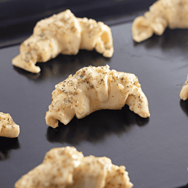 Croissants arranged in a single layer in an air fryer basket, golden and puffed after cooking.