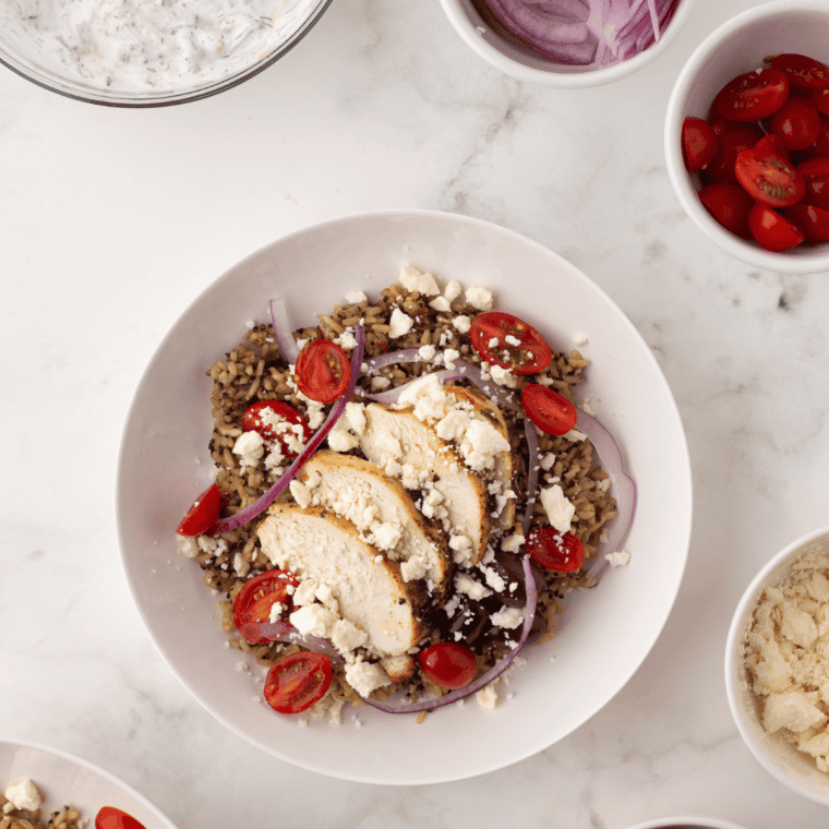 Vibrant Copycat CAVA Bowl with greens, grains, air-fried falafel, fresh vegetables, hummus, tzatziki, harissa, and feta cheese.