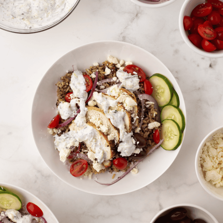 "Homemade Copycat CAVA Bowl featuring air-fried protein, grains, fresh vegetables, hummus, tzatziki, harissa, and feta cheese for a Mediterranean-inspired dish."