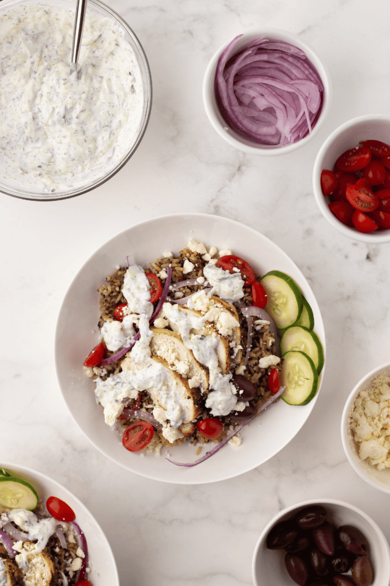 Colorful Copycat CAVA Bowl with fresh greens, grains, air-fried protein, vegetables, hummus, tzatziki, harissa, and crumbled feta cheese.