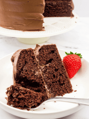 A slice of moist and rich Copycat Portillo’s Chocolate Cake on a white plate, topped with a chocolate glaze and served with a fork.