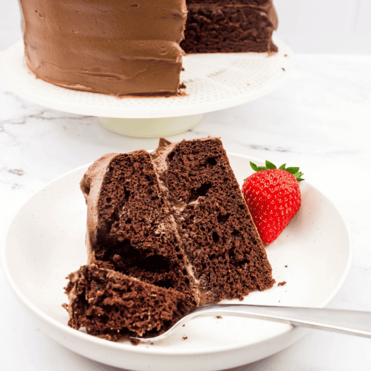 A slice of moist and rich Copycat Portillo’s Chocolate Cake on a white plate, topped with a chocolate glaze and served with a fork.