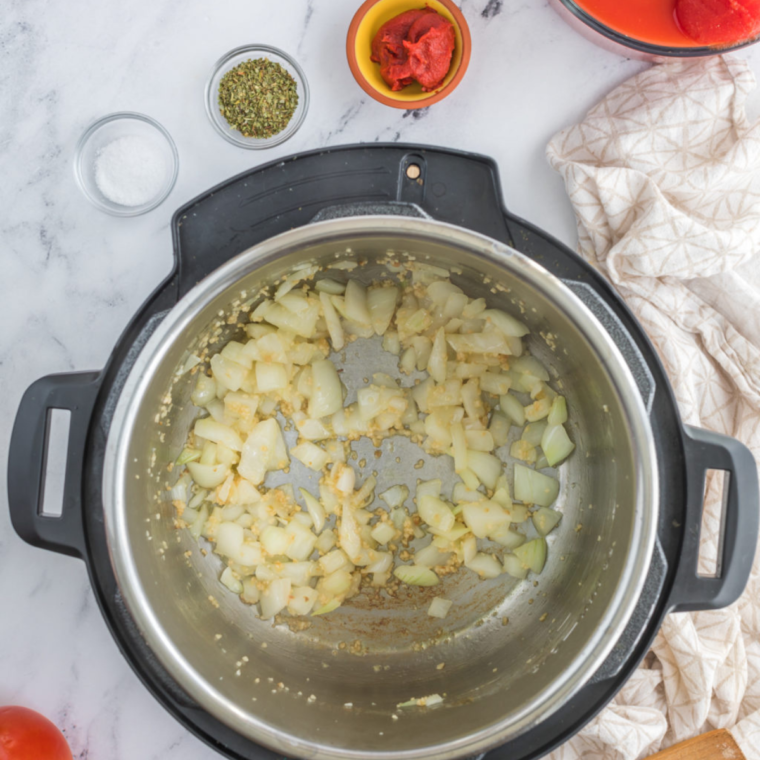 A close-up of diced onions and minced garlic sautéing in olive oil in a large pot.