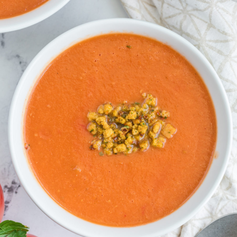 A bowl of Dairy-Free Tomato Basil Soup garnished with fresh basil leaves, served with crusty bread on the side.