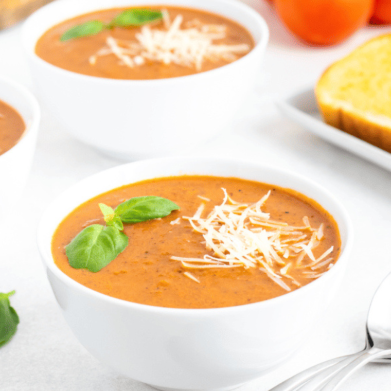 A bowl of creamy Dairy-Free Tomato Basil Soup, garnished with fresh basil leaves, served with a slice of crusty bread.