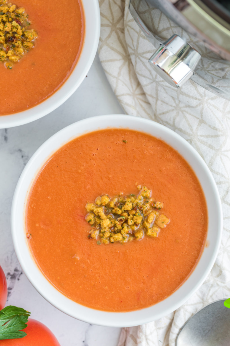 A bowl of Dairy-Free Tomato Basil Soup garnished with fresh basil leaves, with a side of crusty bread for dipping.