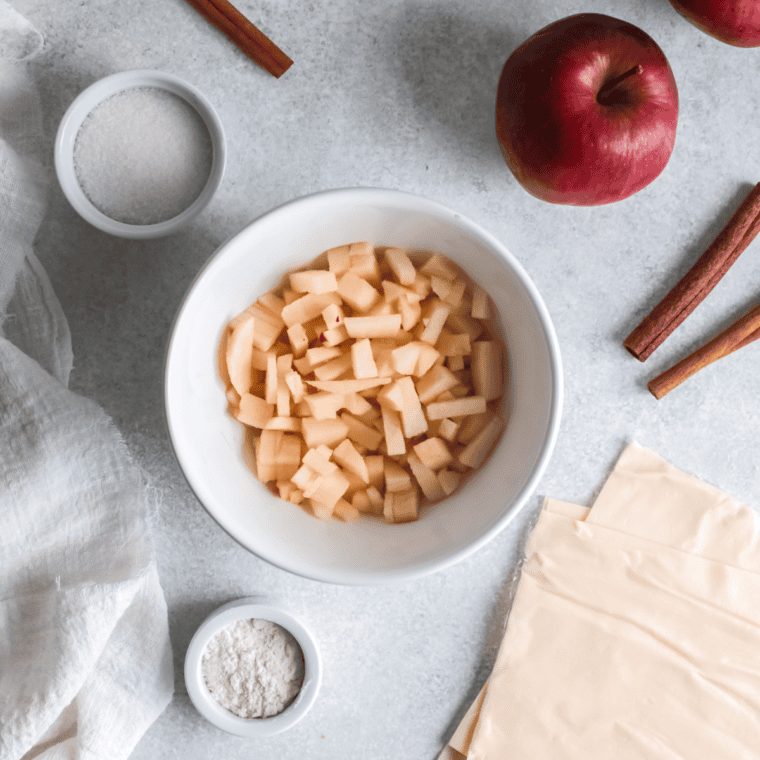 Diced apples cooking in a saucepan with sugar, cinnamon, and butter to create a spiced filling.