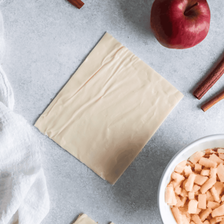 Squares of rolled-out puff pastry with apple filling spooned onto the center of each piece.