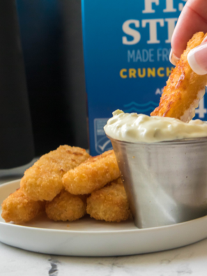 A bowl of homemade McDonald’s tartar sauce with a creamy texture, garnished with fresh parsley, next to a plate of fish fillets.