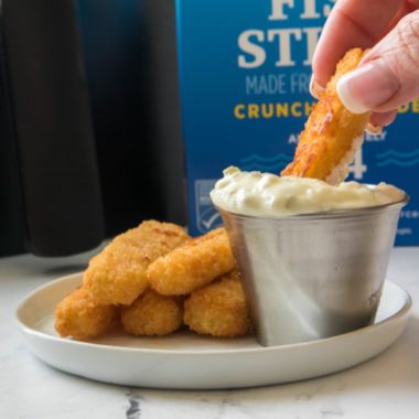 A bowl of homemade McDonald’s tartar sauce with a creamy texture, garnished with fresh parsley, next to a plate of fish fillets.