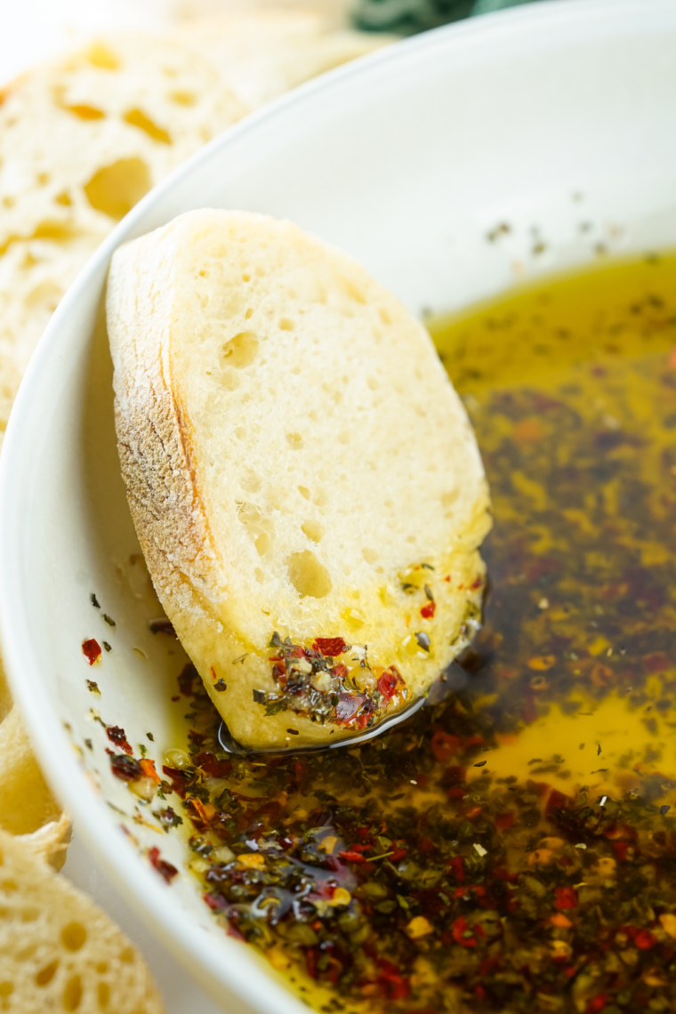 A small bowl of Mediterranean bread dipping oil with olive oil, balsamic vinegar, garlic, herbs, and spices, served with crusty bread for dipping.