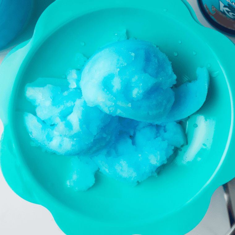 Bright blue Ninja Creami Blue Raspberry Italian Ice served in a glass bowl, garnished with fresh raspberries and a spoon.