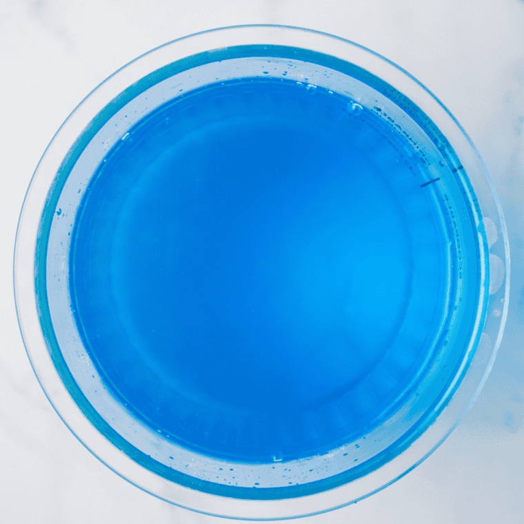 Mixing water, blue raspberry syrup, and sugar in a bowl until the sugar is fully dissolved.