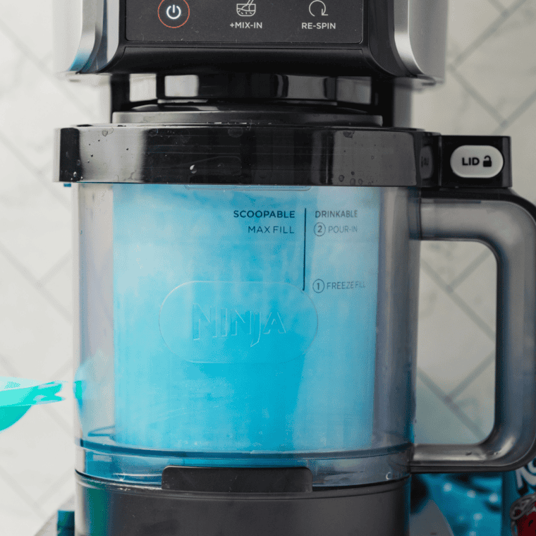 Pouring the blue raspberry mixture into a Ninja Creami pint container, securing the lid, and placing it in the freezer.