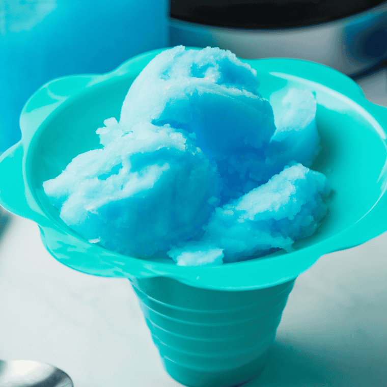 Bright blue Ninja Creami Blue Raspberry Italian Ice served in a bowl, with a spoon and garnished with fresh raspberries.