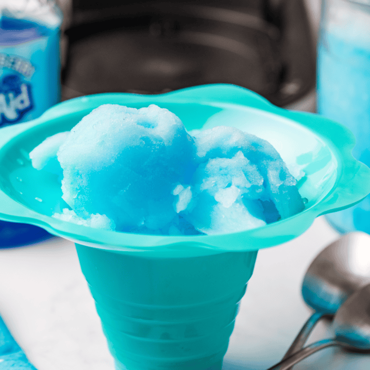 A vibrant blue bowl of Ninja Creami Blue Raspberry Italian Ice served in a glass dish, garnished with fresh raspberries and a spoon.