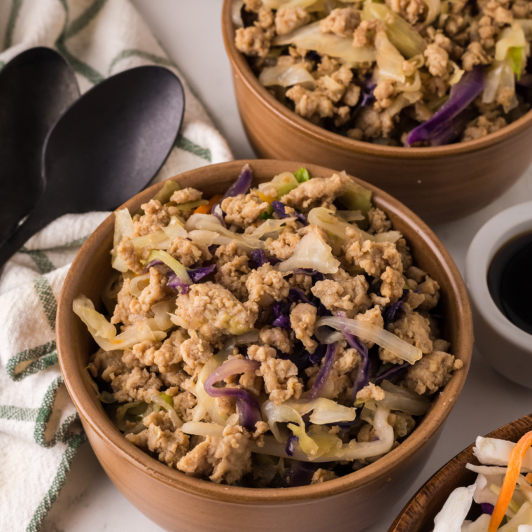 A bowl of Ninja Foodi Chicken Egg Roll Bowls with vegetables, chicken, and a savory sauce, garnished with green onions.