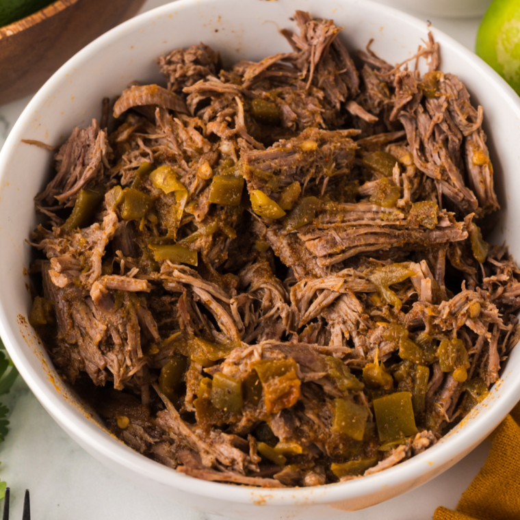 Ninja Foodi Barbacoa Beef in a bowl, showcasing tender, shredded beef with a rich, flavorful sauce, served with cilantro and lime wedges.