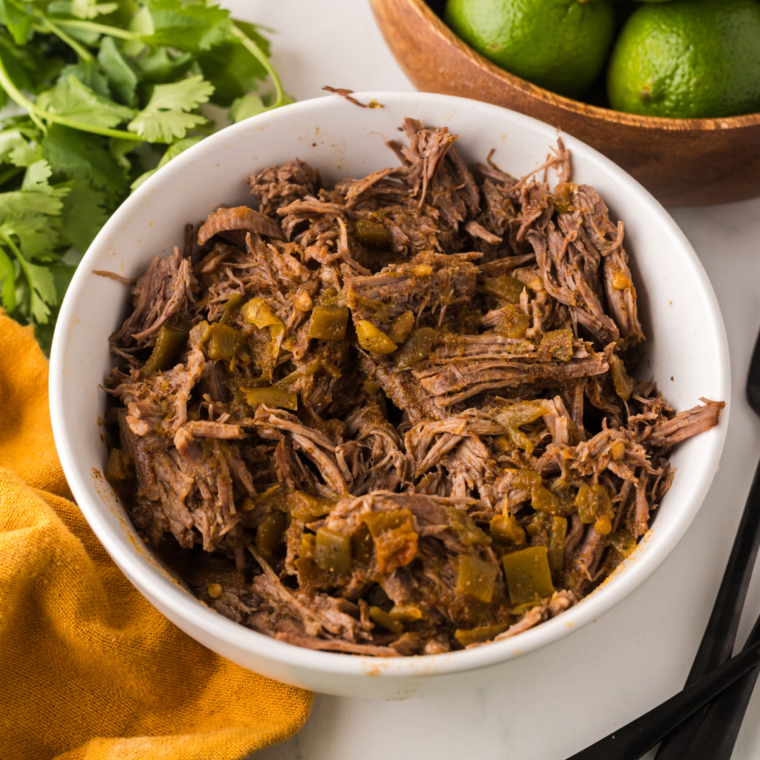 Ninja Foodi Barbacoa Beef with tender, shredded beef in a flavorful sauce, garnished with cilantro and served with lime wedges.