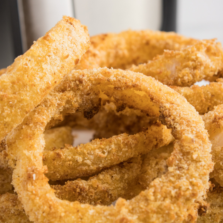 A stack of golden, crispy onion rings arranged in a tower, served with dipping sauces on the side.