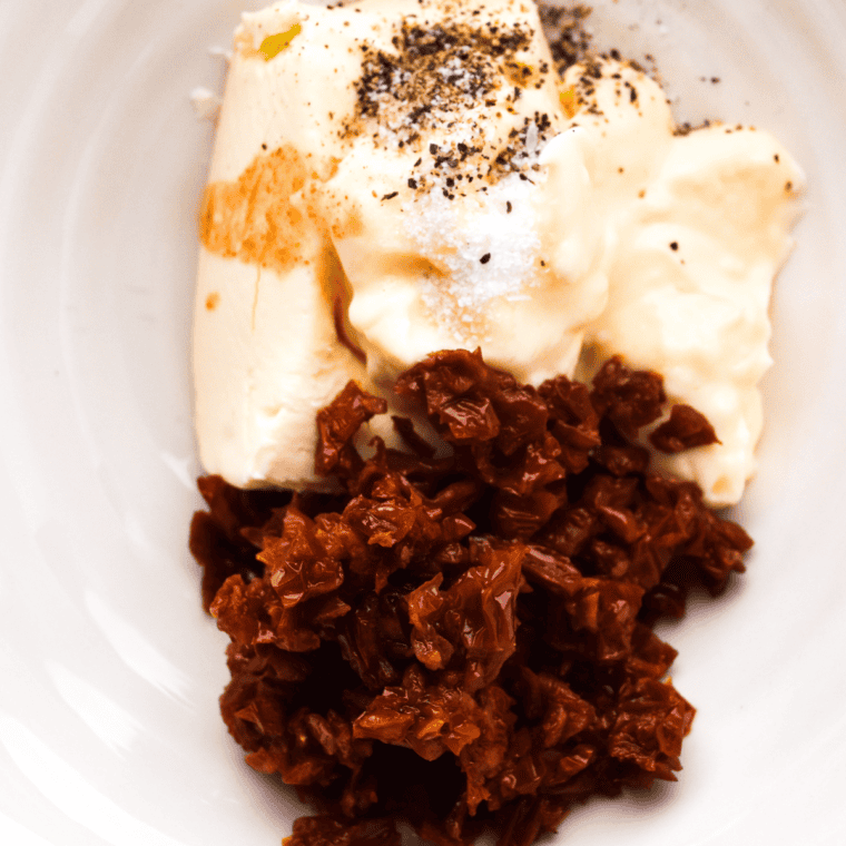 Mixing cream cheese, sun-dried tomatoes, mayonnaise, Tabasco sauce, salt, and pepper in a bowl to make a smooth sun-dried tomato spread.