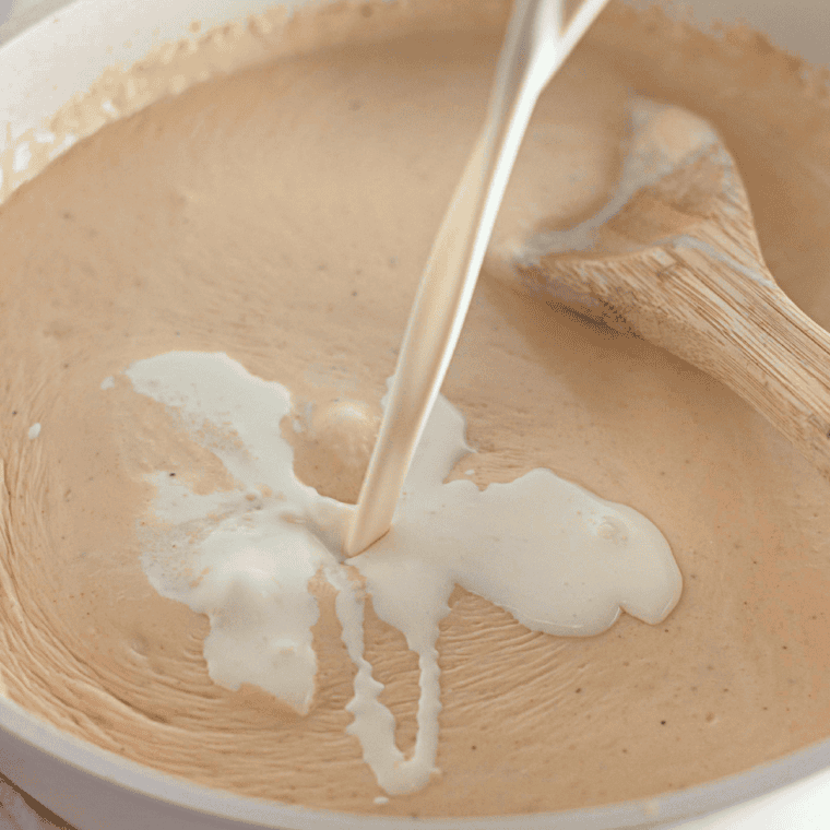 Gradually pouring milk into the roux while whisking to create a smooth, thickened cheese sauce.