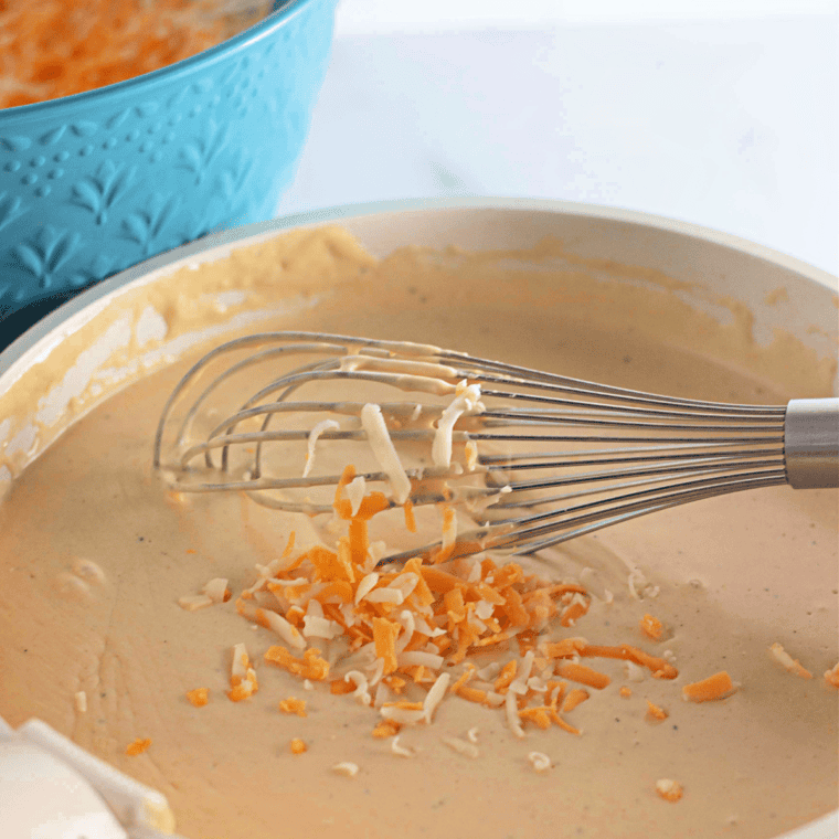 Stirring in shredded cheddar cheese, cream cheese, and seasonings to make a rich and creamy cheese sauce.