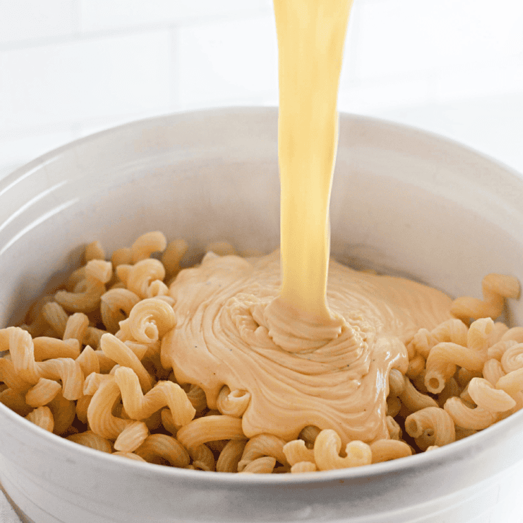 Mixing cooked elbow macaroni into the creamy cheese sauce to coat the pasta evenly.