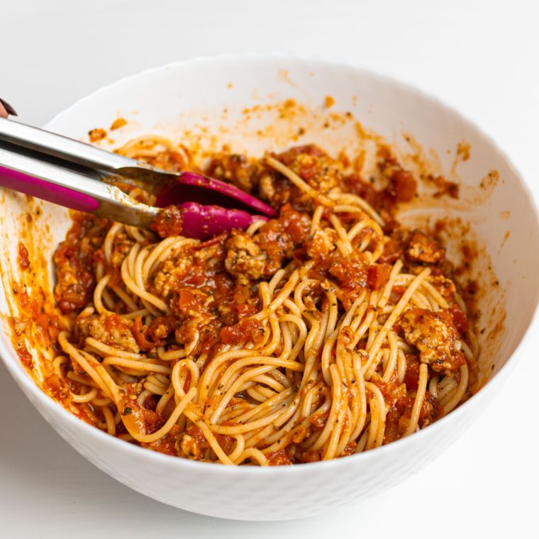 Mixing cooked spaghetti with marinara sauce and ricotta cheese in a large bowl.