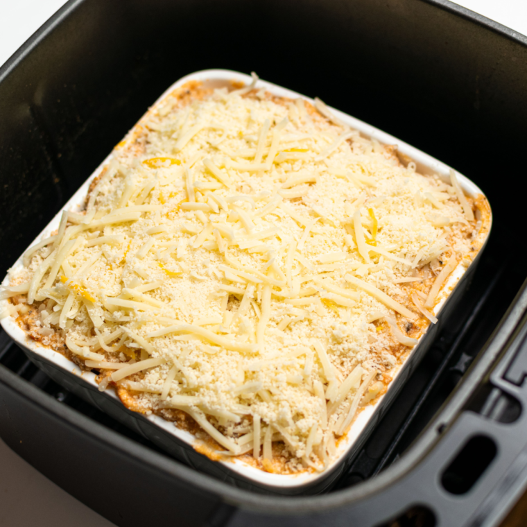 Baked spaghetti in an air fryer with melted, golden cheese, garnished with fresh parsley.