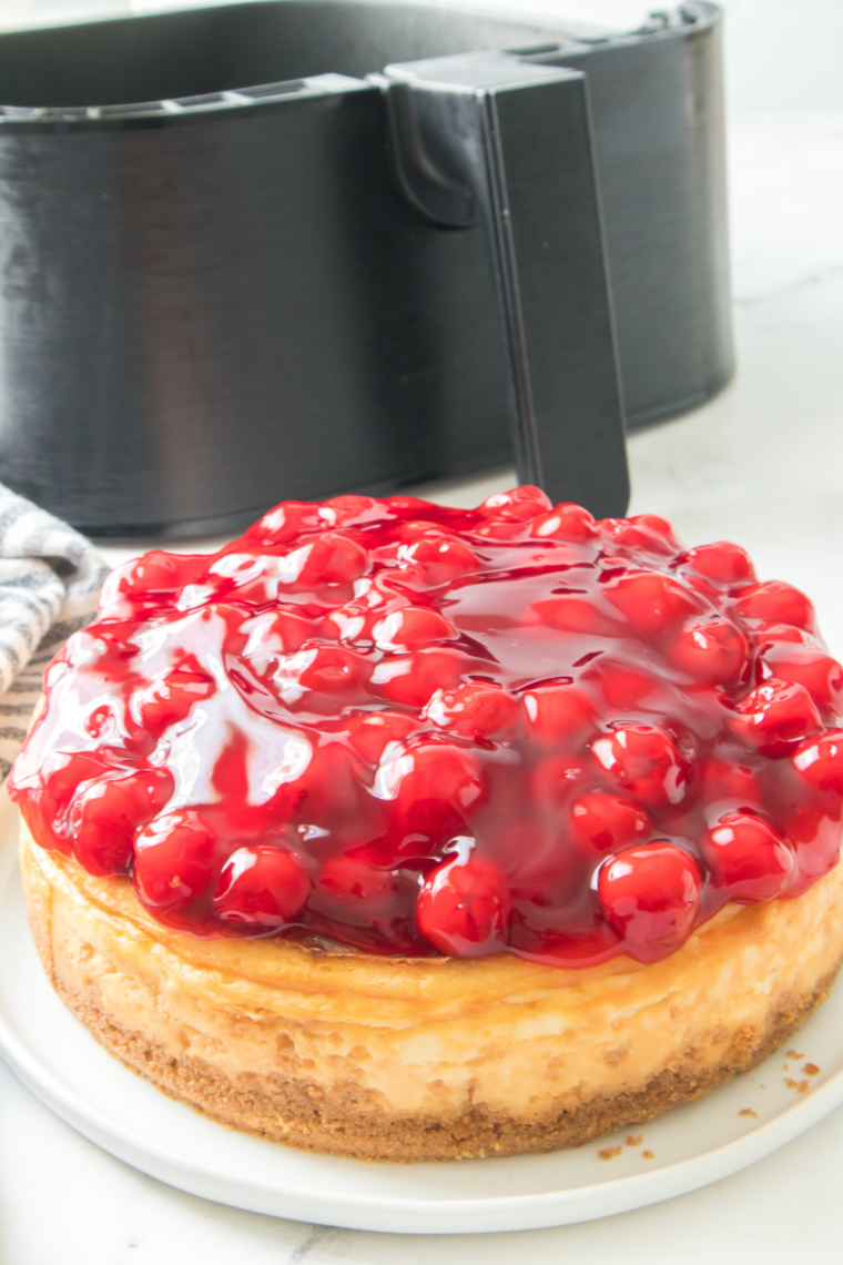 "Air Fryer Cherry Cheesecake topped with a glossy cherry filling, served on a white plate."