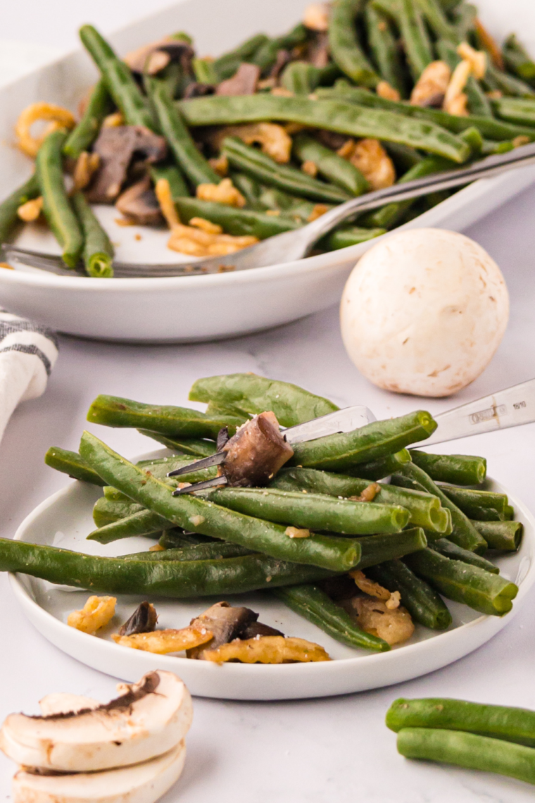 A plate of air-fried green beans with mushrooms and onions, garnished and perfectly crispy, ready to serve as a delicious side dish.