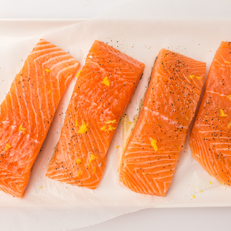 Salmon fillets seasoned with olive oil, garlic powder, salt, pepper, and lemon juice, resting to absorb the flavors.
