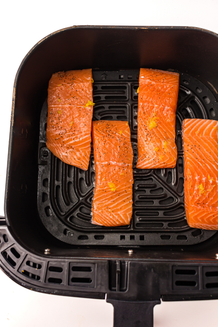 Salmon fillets placed in an air fryer basket, preheated to 400°F, cooking until crispy on the outside and tender inside.