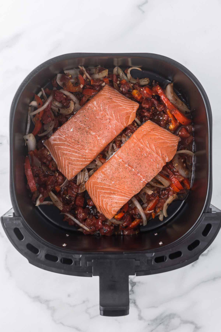 Adding salmon fillets to the vegetable mixture and cooking for 10 minutes, garnished with fresh basil.