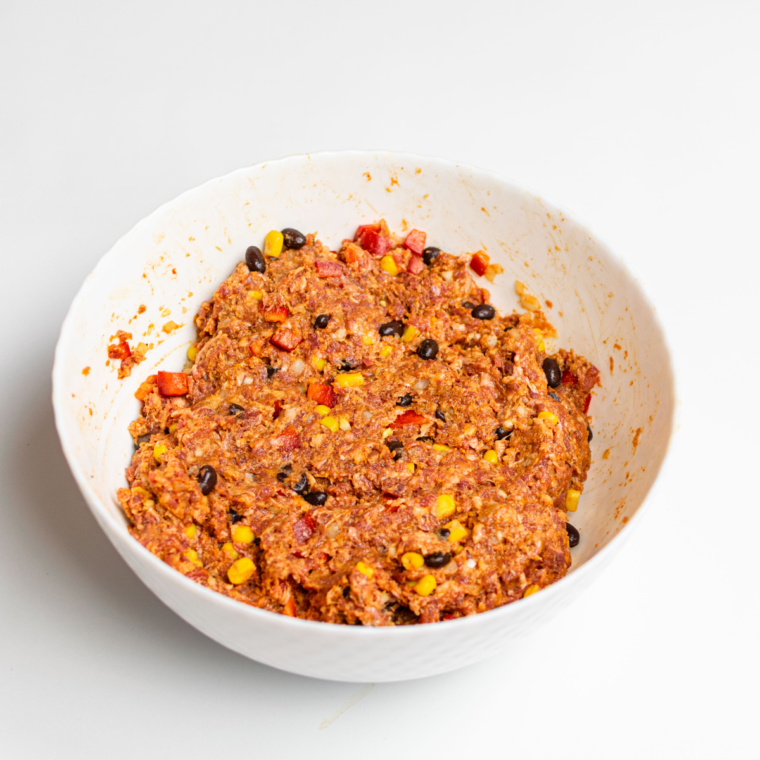 Mixing ground beef, breadcrumbs, onions, bell peppers, corn, black beans, egg, and seasonings in a large bowl for a Southwest-style meatloaf.