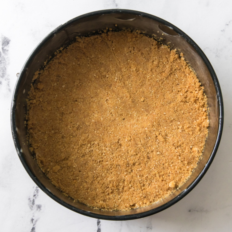 Pressed graham cracker mixture into the bottom of a greased springform pan to form an even crust.