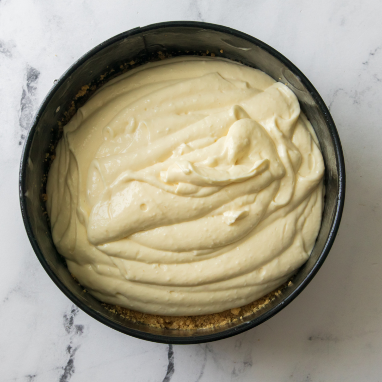 Pouring cheesecake filling over graham cracker crust and smoothing the top with a spatula for an even layer.