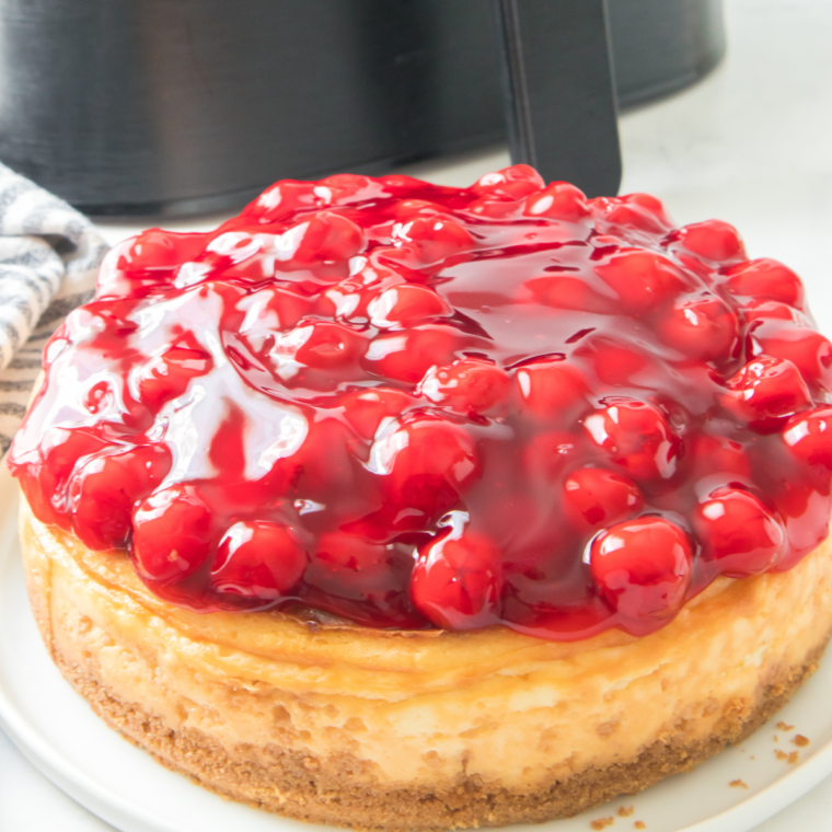 Air Fryer Cherry Cheesecake with a creamy filling, topped with a glossy cherry topping, served on a white plate.