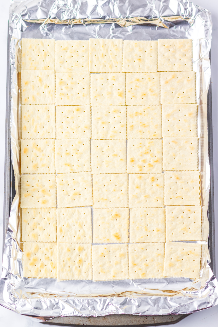 A baking sheet lined with foil, covered neatly with saltine crackers arranged edge to edge.