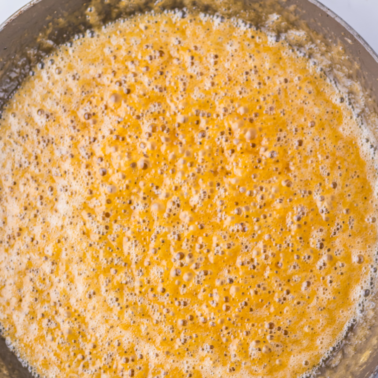 Caramel mixture being poured evenly over saltine crackers on the baking sheet.