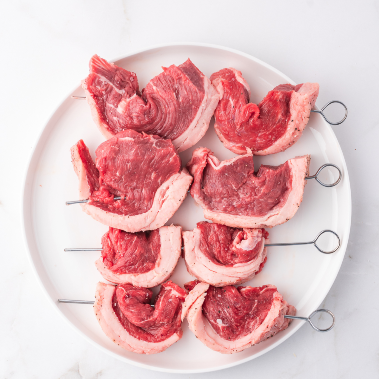 Shaping picanha pieces into a C curve and threading onto metal skewers for cooking."