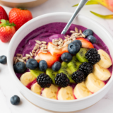 "Vibrant dragonfruit yogurt smoothie bowl topped with fresh fruit, granola, and seeds, beautifully presented in a white bowl on a rustic wooden table."