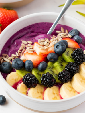 "Vibrant dragonfruit yogurt smoothie bowl topped with fresh fruit, granola, and seeds, beautifully presented in a white bowl on a rustic wooden table."